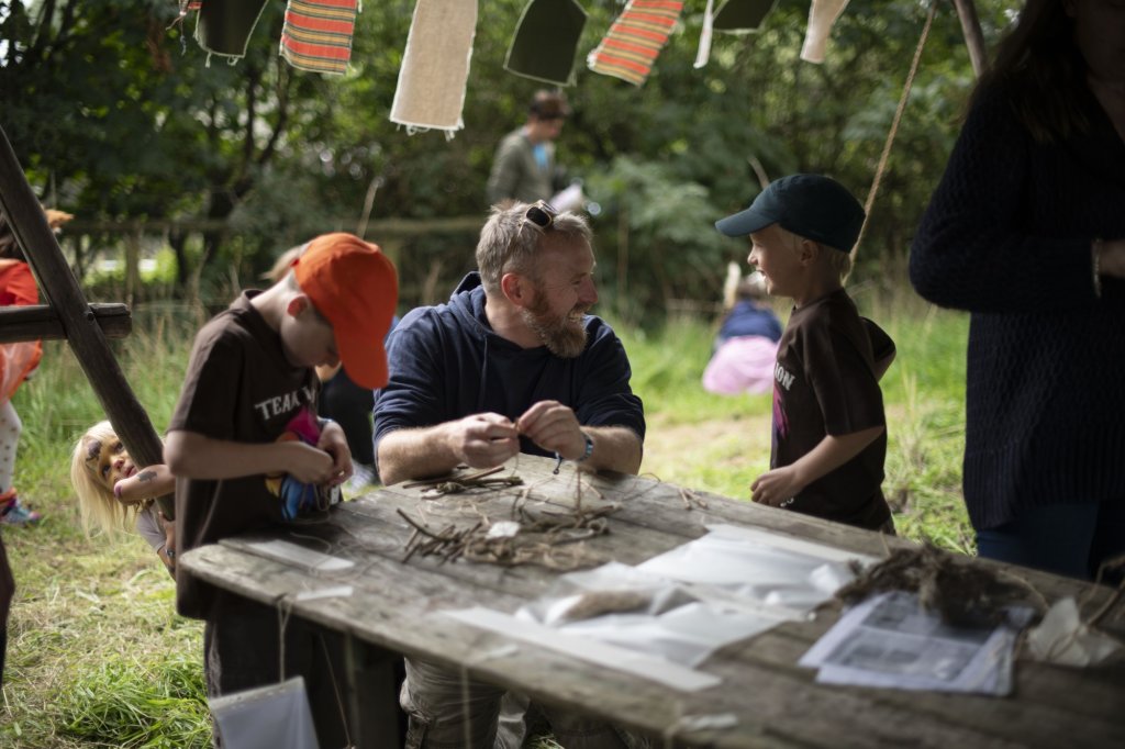 A man working with happy children to create nature-based crafts.